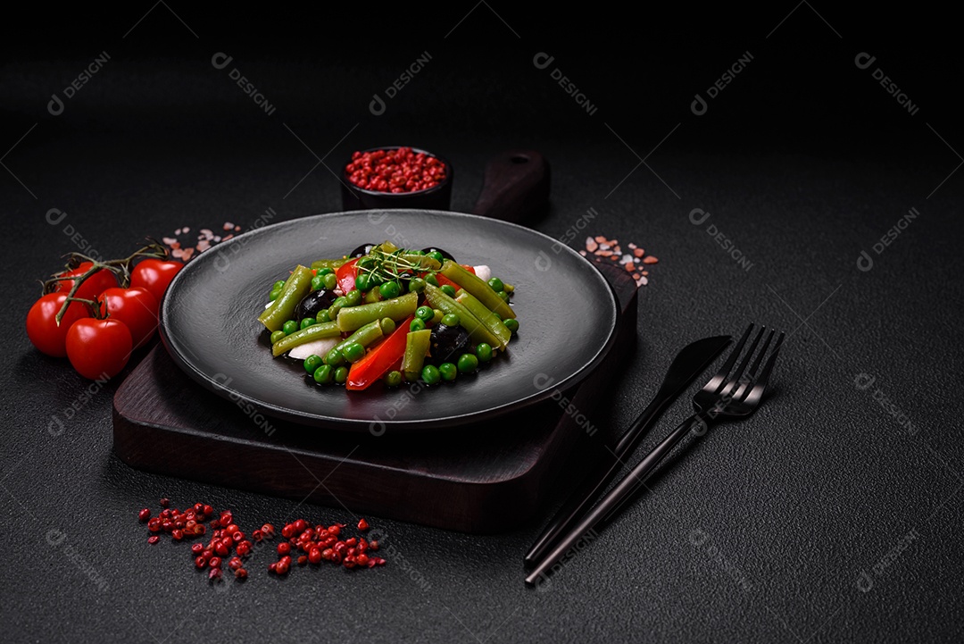 Deliciosa salada fresca de feijão verde, ervilha, pimentão e queijo com sal e especiarias sobre um fundo escuro de concreto