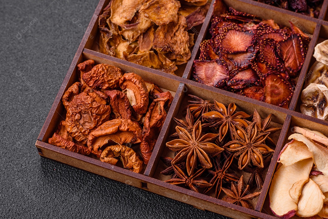 Variação de frutas secas morango, maçã, cereja, banana, pêssego, ameixa e anis estrelado em uma caixa sobre fundo escuro de concreto