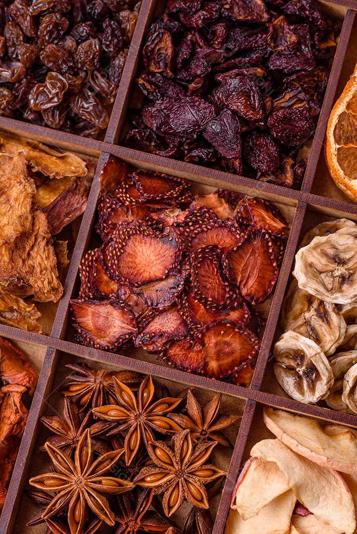 Variação de frutas secas morango, maçã, cereja, banana, pêssego, ameixa e anis estrelado em uma caixa sobre fundo escuro de concreto