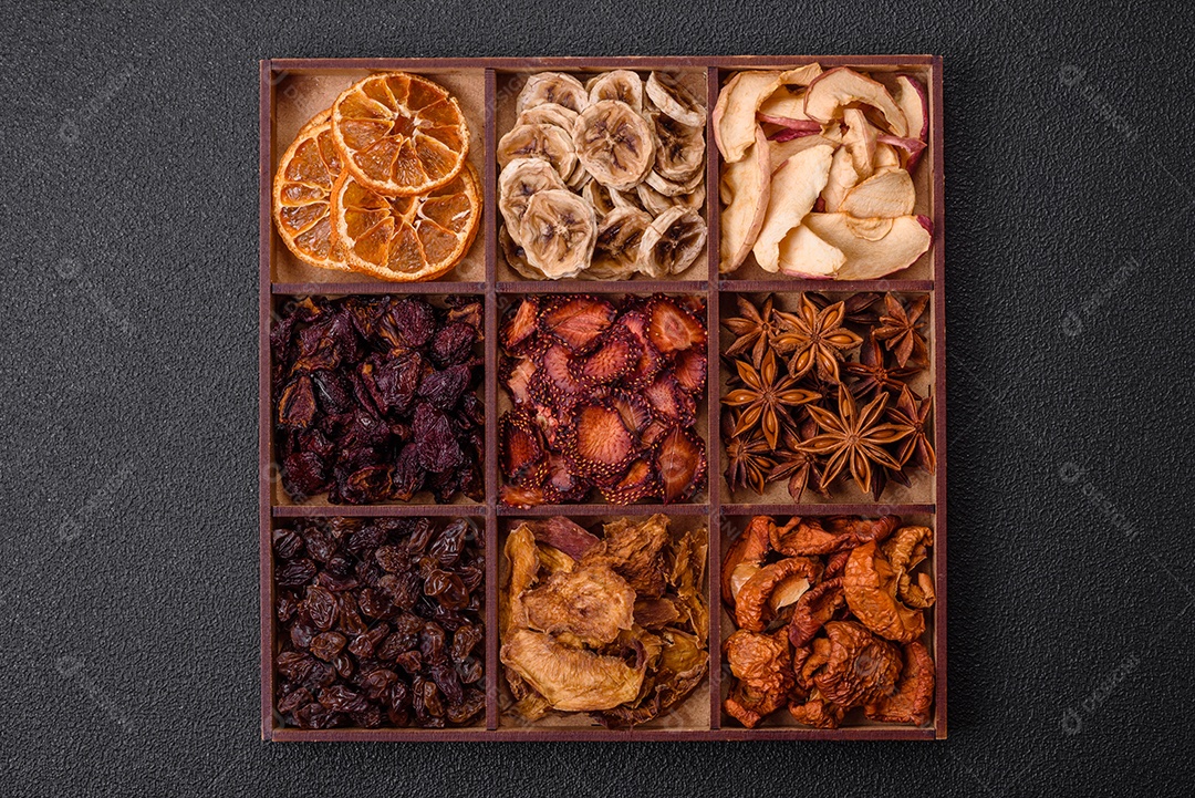 Variação de frutas secas morango, maçã, cereja, banana, pêssego, ameixa e anis estrelado em uma caixa sobre fundo escuro de concreto