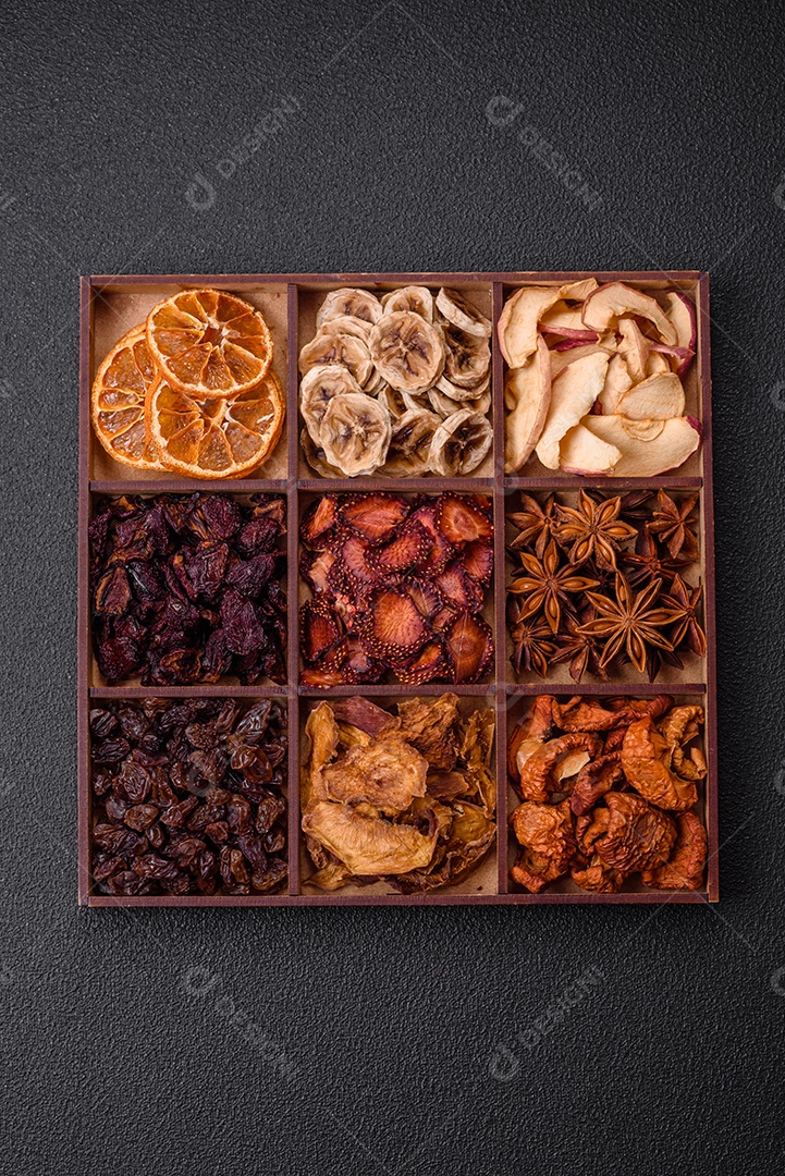 Variação de frutas secas morango, maçã, cereja, banana, pêssego, ameixa e anis estrelado em uma caixa sobre fundo escuro de concreto