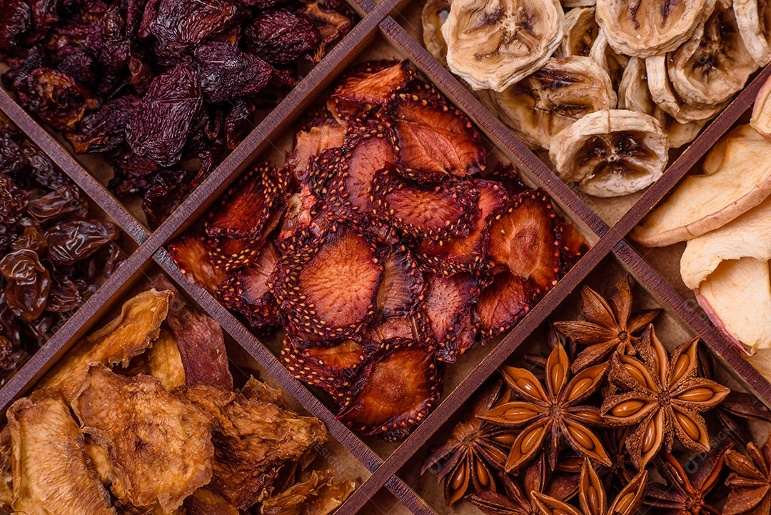 Variação de frutas secas morango, maçã, cereja, banana, pêssego, ameixa e anis estrelado em uma caixa sobre fundo escuro de concreto