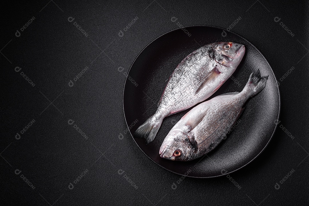 Peixe dorada cru fresco com sal, especiarias e ervas sobre um fundo escuro de concreto