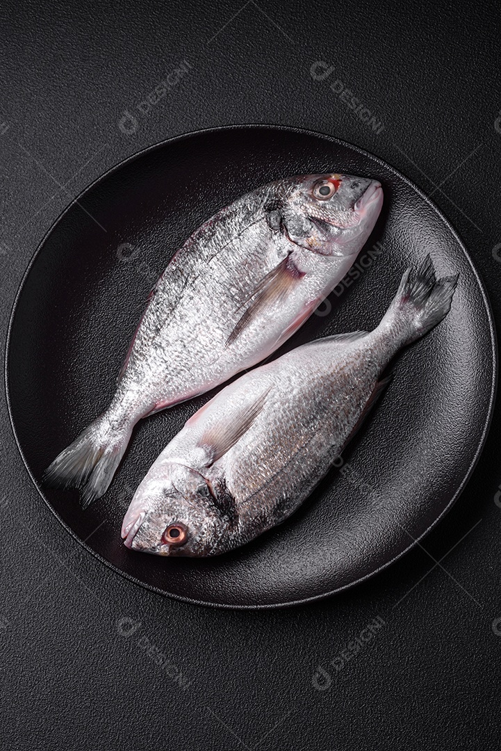 Peixe dorada cru fresco com sal, especiarias e ervas sobre um fundo escuro de concreto