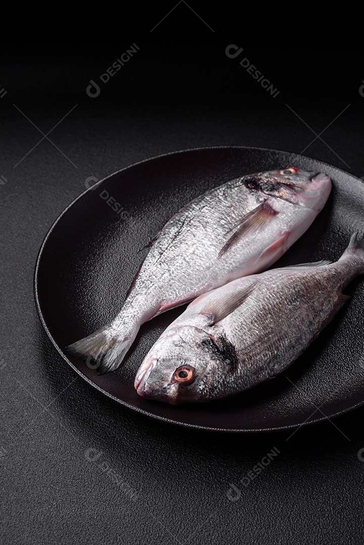 Peixe dorada cru fresco com sal, especiarias e ervas sobre um fundo escuro de concreto