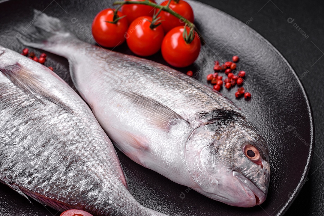 Peixe dorada cru fresco com sal, especiarias e ervas sobre um fundo escuro de concreto
