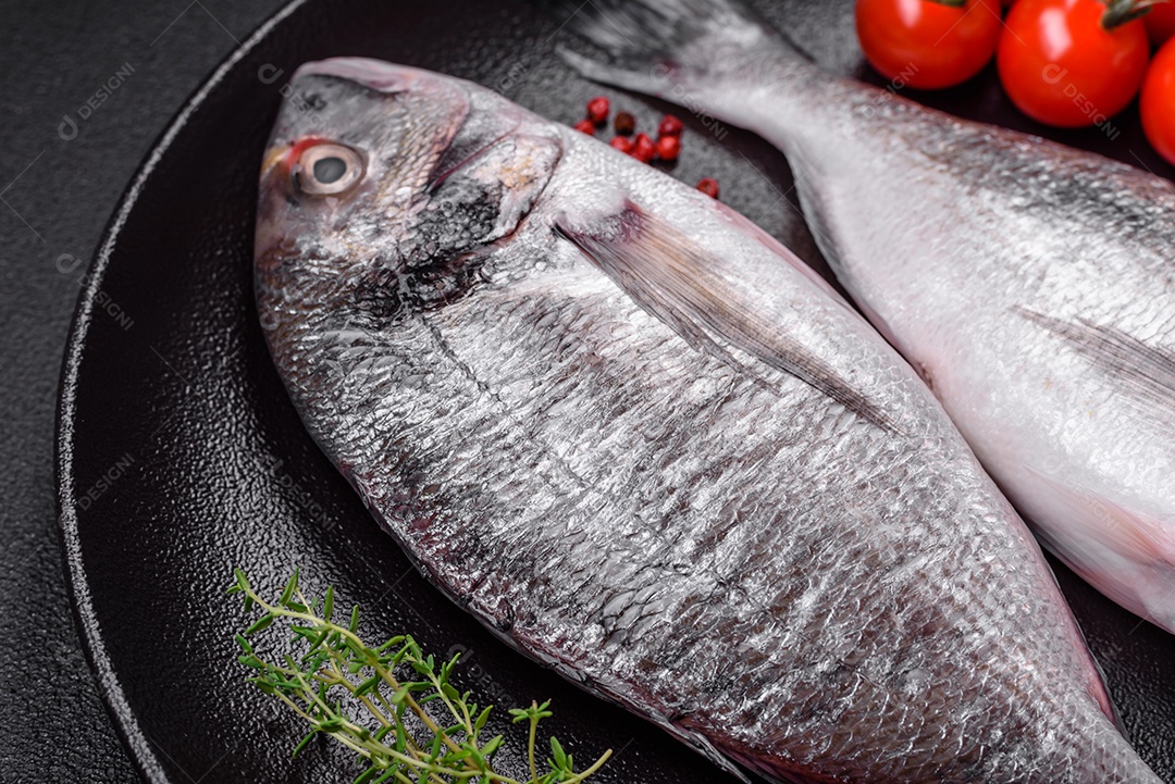 Peixe dorada cru fresco com sal, especiarias e ervas sobre um fundo escuro de concreto