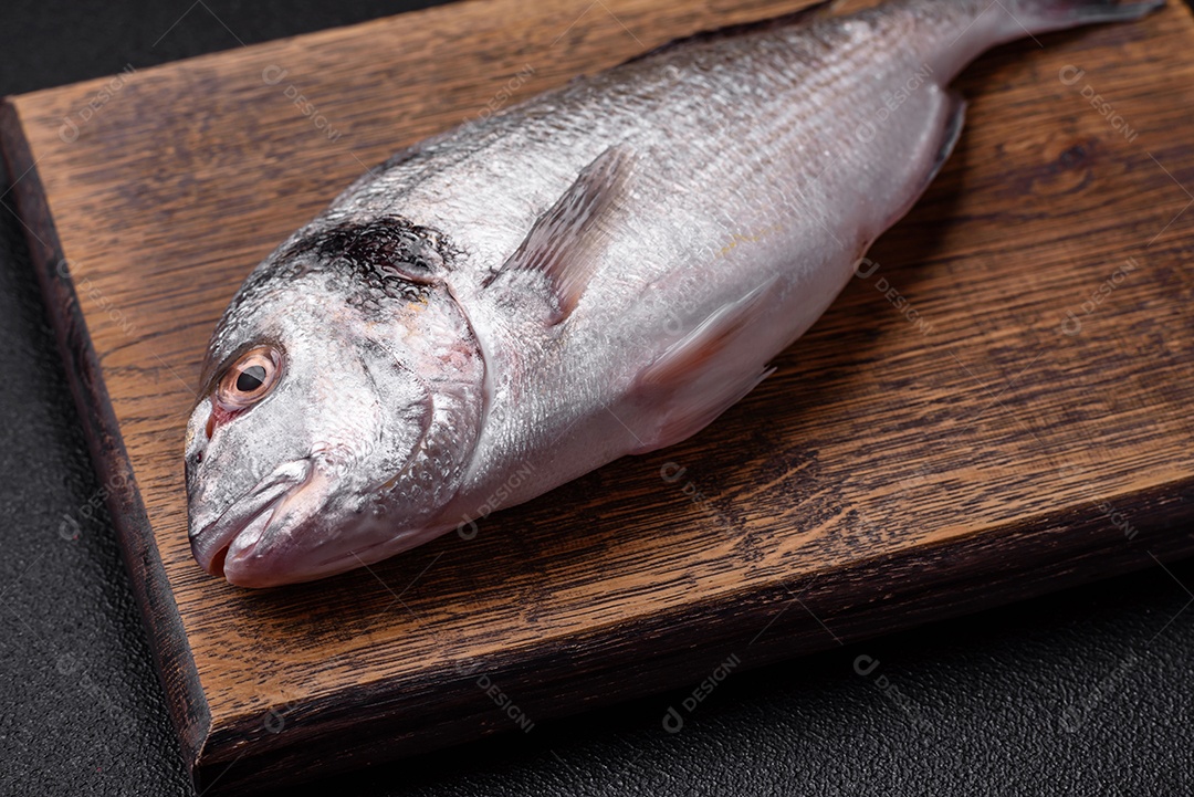 Peixe dorada cru fresco com sal, especiarias e ervas sobre um fundo escuro de concreto