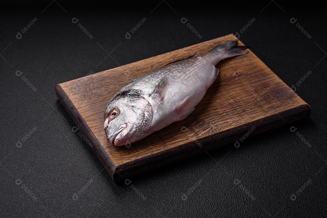 Peixe dorada cru fresco com sal, especiarias e ervas sobre um fundo escuro de concreto