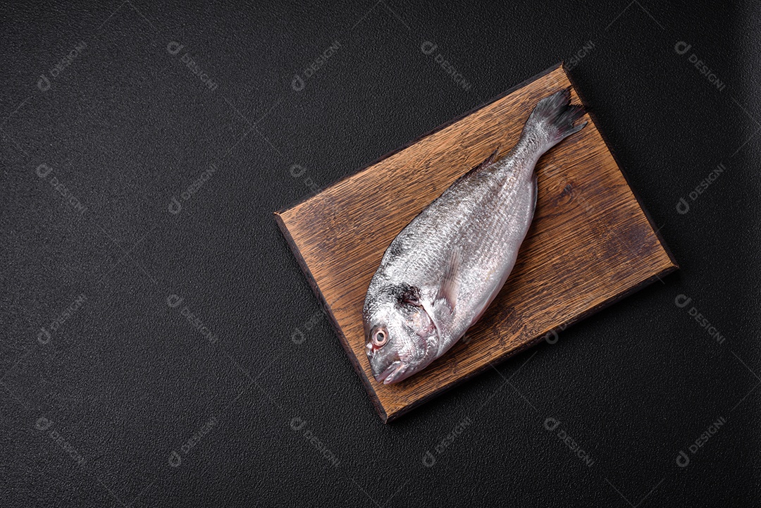 Peixe dorada cru fresco com sal, especiarias e ervas sobre um fundo escuro de concreto