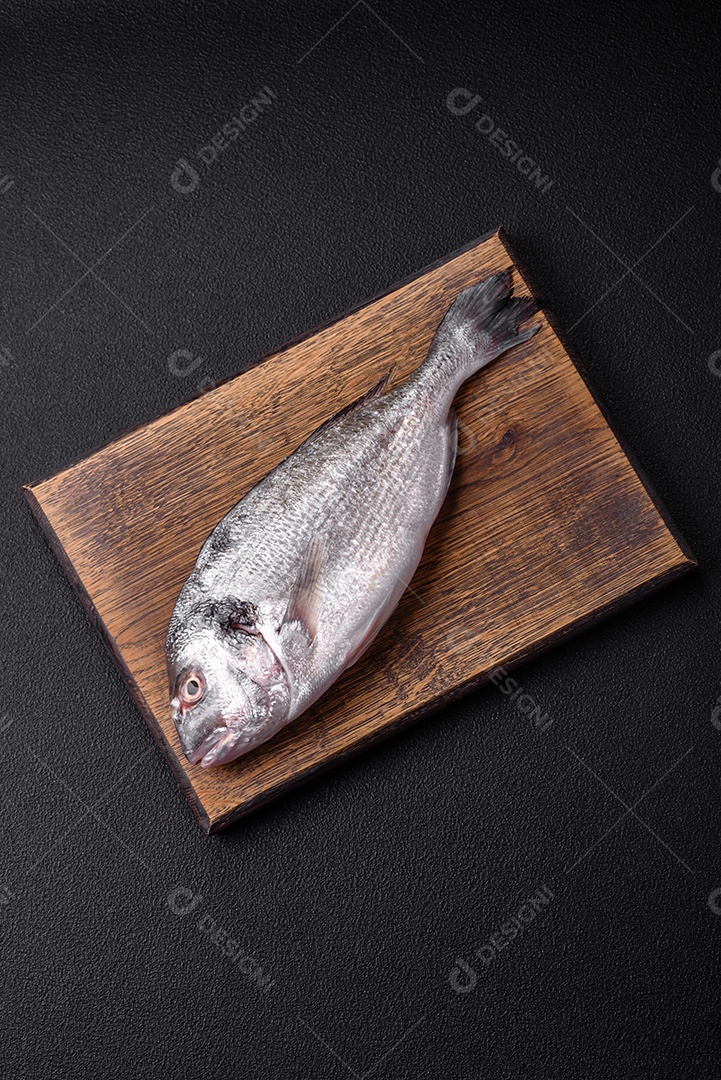 Peixe dorada cru fresco com sal, especiarias e ervas sobre um fundo escuro de concreto