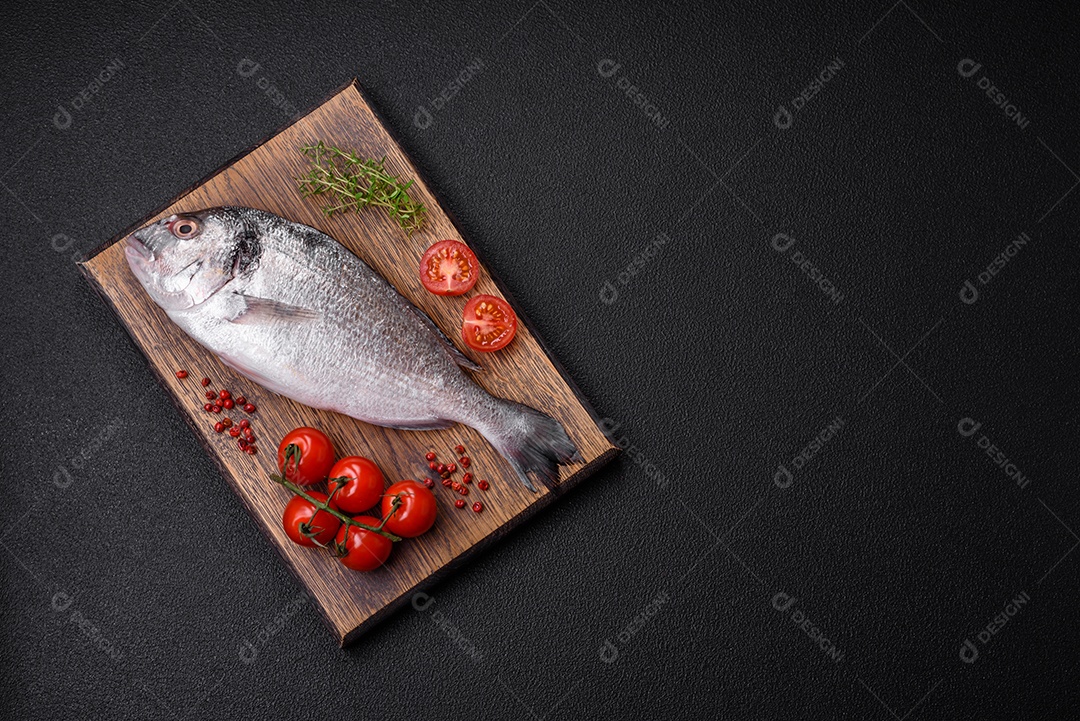 Peixe dorada cru fresco com sal, especiarias e ervas sobre um fundo escuro de concreto