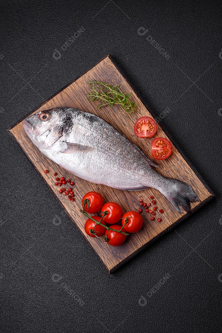 Peixe dorada cru fresco com sal, especiarias e ervas sobre um fundo escuro de concreto