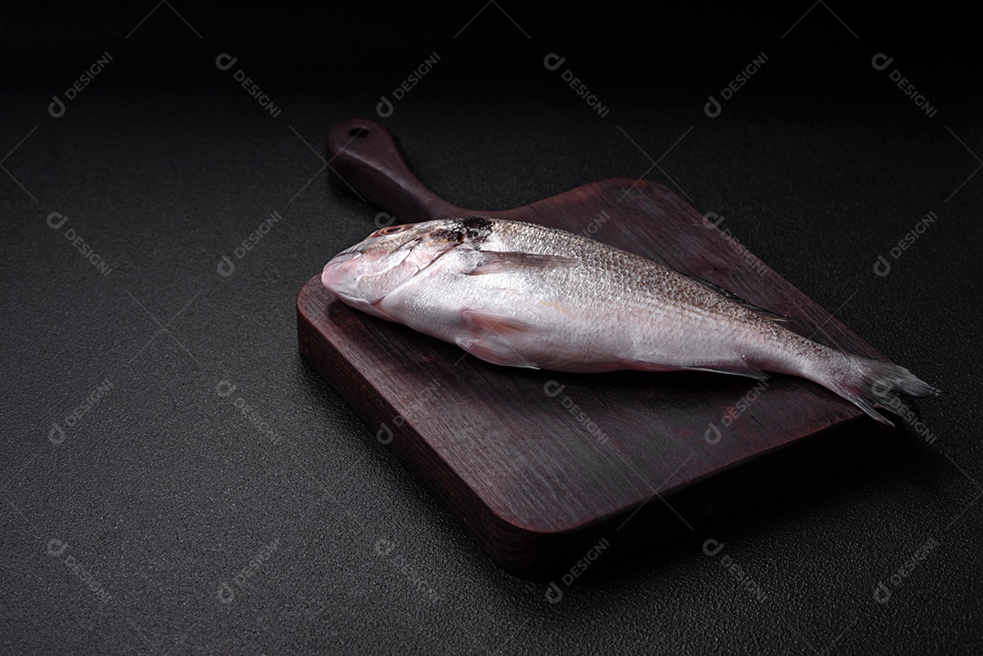 Peixe dorada cru fresco com sal, especiarias e ervas sobre um fundo escuro de concreto