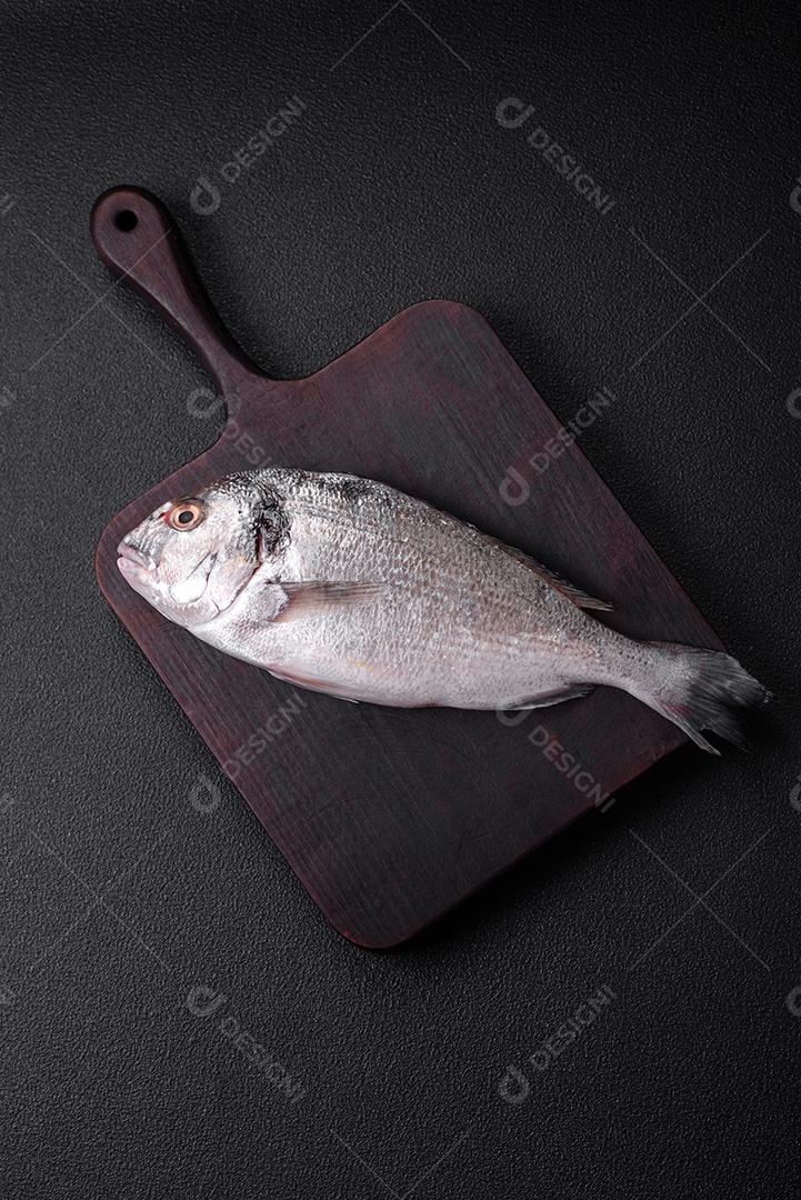 Peixe dorada cru fresco com sal, especiarias e ervas sobre um fundo escuro de concreto