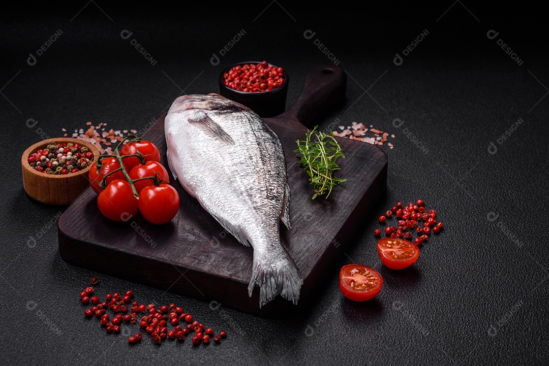 Peixe dorada cru fresco com sal, especiarias e ervas sobre um fundo escuro de concreto