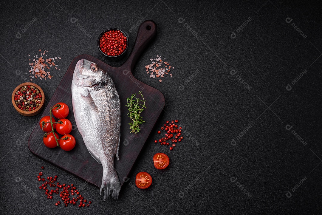 Peixe dorada cru fresco com sal, especiarias e ervas sobre um fundo escuro de concreto
