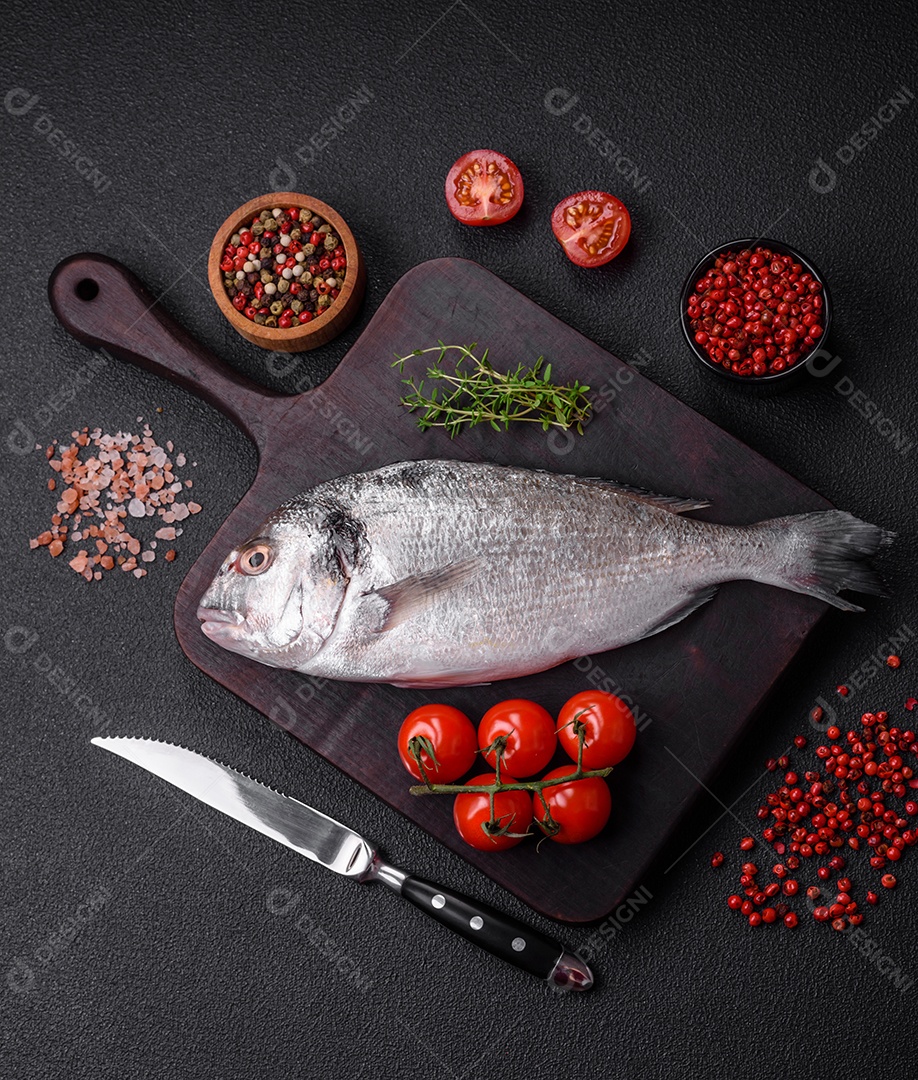 Peixe dorada cru fresco com sal, especiarias e ervas sobre um fundo escuro de concreto
