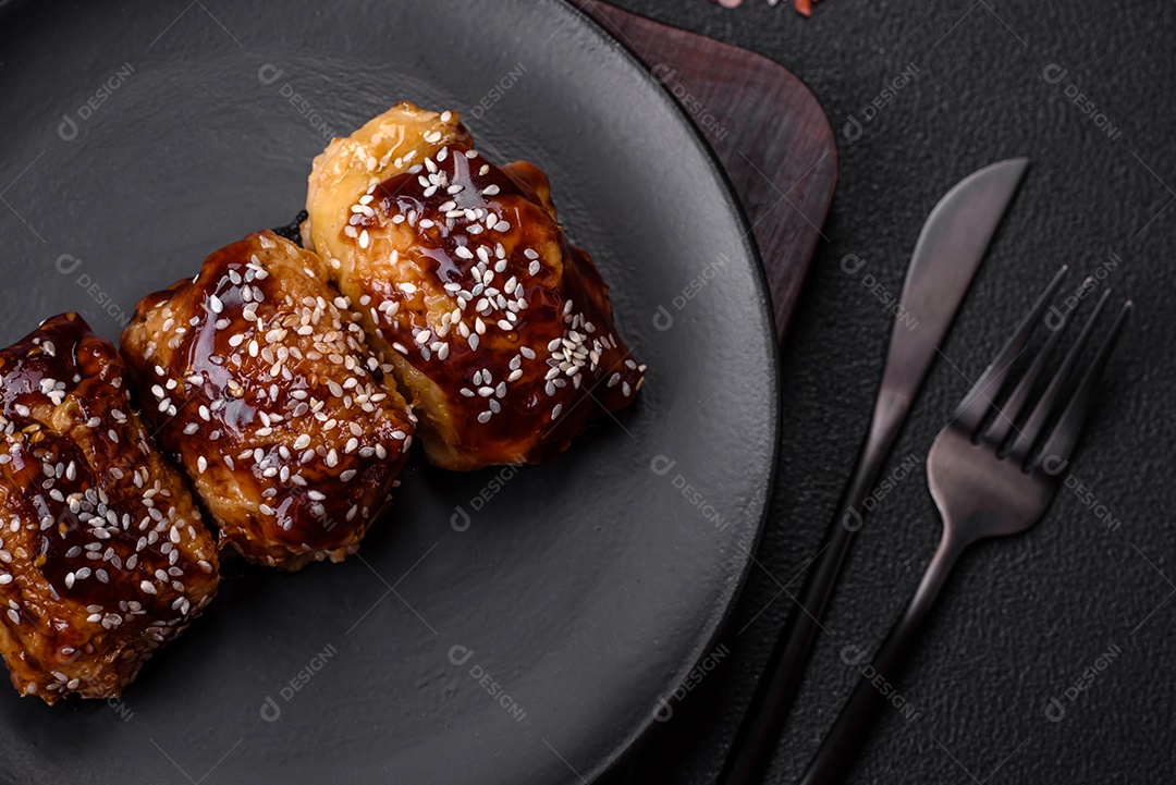 Delicioso frango frito suculento com molho teriyaki agridoce e sementes de gergelim em um fundo escuro de concreto