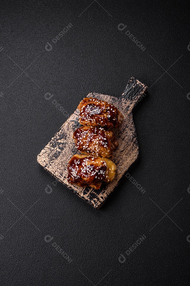 Delicioso frango frito suculento com molho teriyaki agridoce e sementes de gergelim em um fundo escuro de concreto