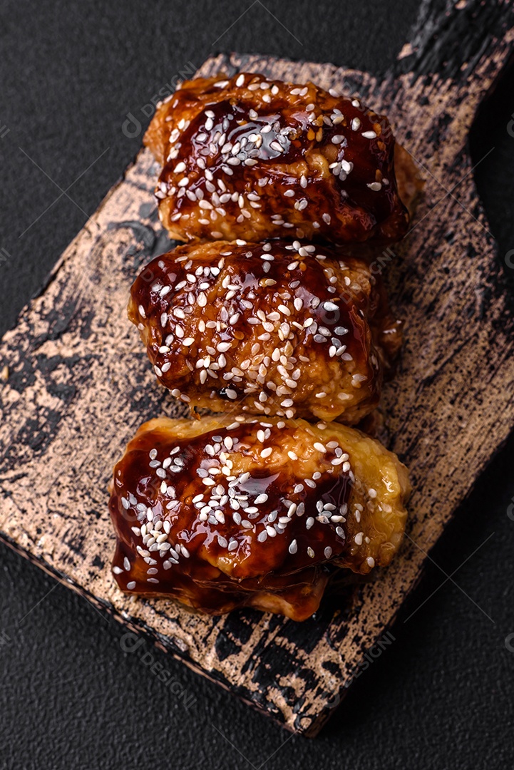 Delicioso frango frito suculento com molho teriyaki agridoce e sementes de gergelim em um fundo escuro de concreto