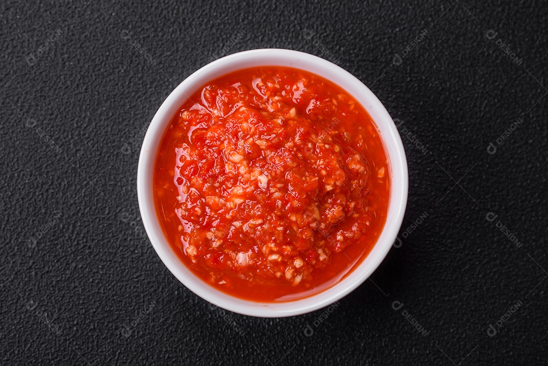Delicioso molho vermelho picante com sal e especiarias em uma tigela de cerâmica sobre um fundo escuro de concreto