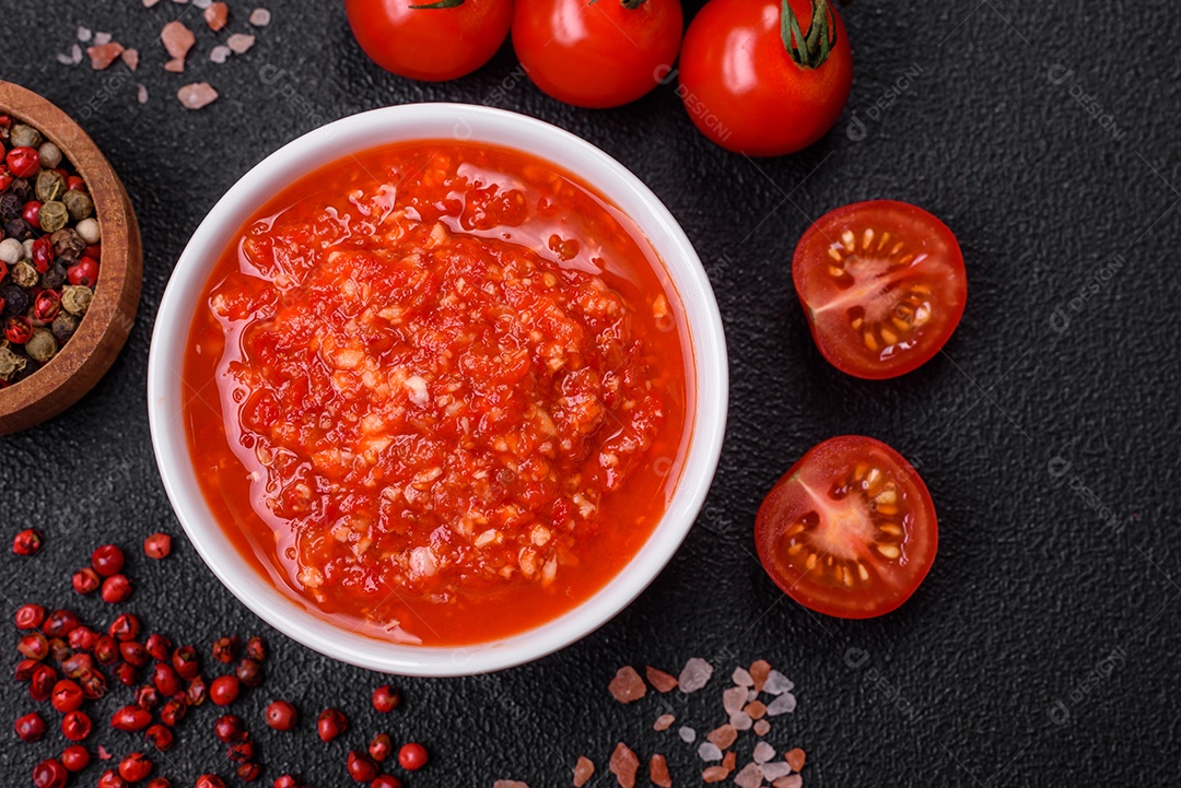 Delicioso molho vermelho picante com sal e especiarias em uma tigela de cerâmica sobre um fundo escuro de concreto