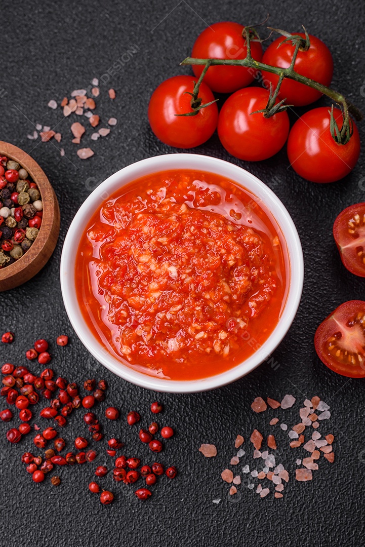 Delicioso molho vermelho picante com sal e especiarias em uma tigela de cerâmica sobre um fundo escuro de concreto