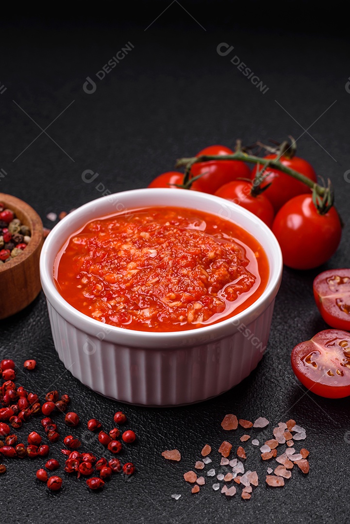 Delicioso molho vermelho picante com sal e especiarias em uma tigela de cerâmica sobre um fundo escuro de concreto