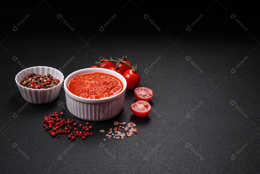 Delicioso molho vermelho picante com sal e especiarias em uma tigela de cerâmica sobre um fundo escuro de concreto