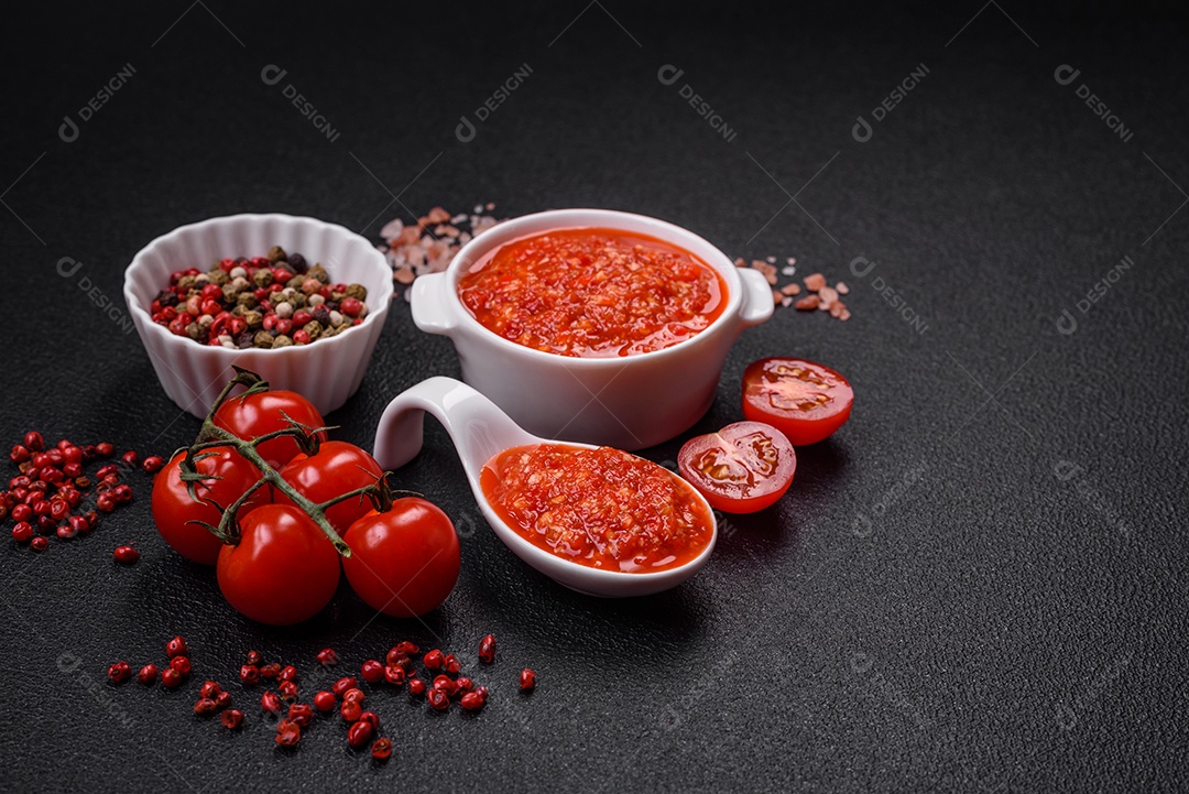 Delicioso molho vermelho picante com sal e especiarias em uma tigela de cerâmica sobre um fundo escuro de concreto