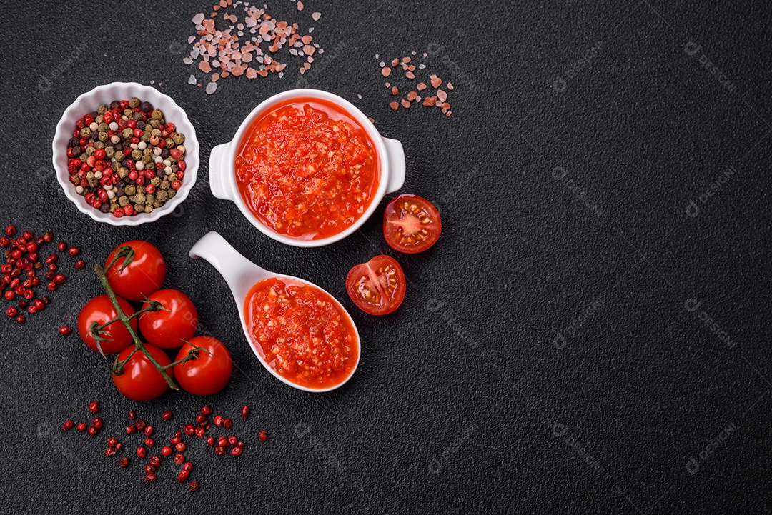 Delicioso molho vermelho picante com sal e especiarias em uma tigela de cerâmica sobre um fundo escuro de concreto