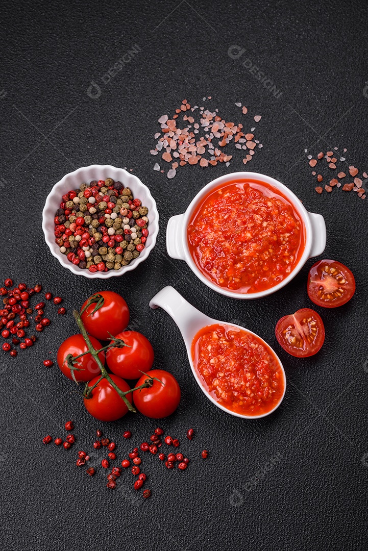 Delicioso molho vermelho picante com sal e especiarias em uma tigela de cerâmica sobre um fundo escuro de concreto