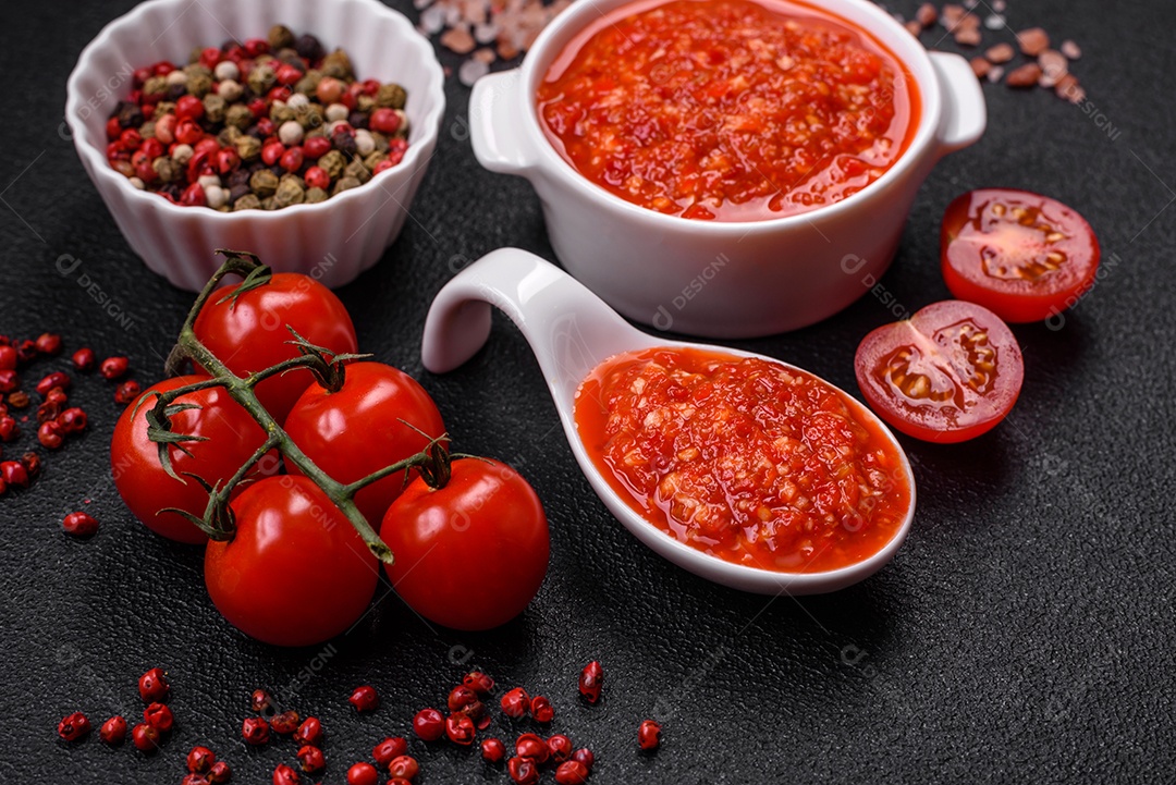 Delicioso molho vermelho picante com sal e especiarias em uma tigela de cerâmica sobre um fundo escuro de concreto
