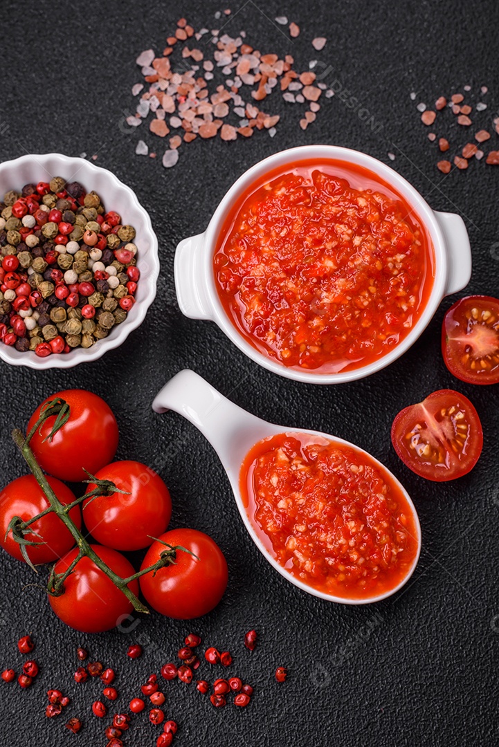 Delicioso molho vermelho picante com sal e especiarias em uma tigela de cerâmica sobre um fundo escuro de concreto