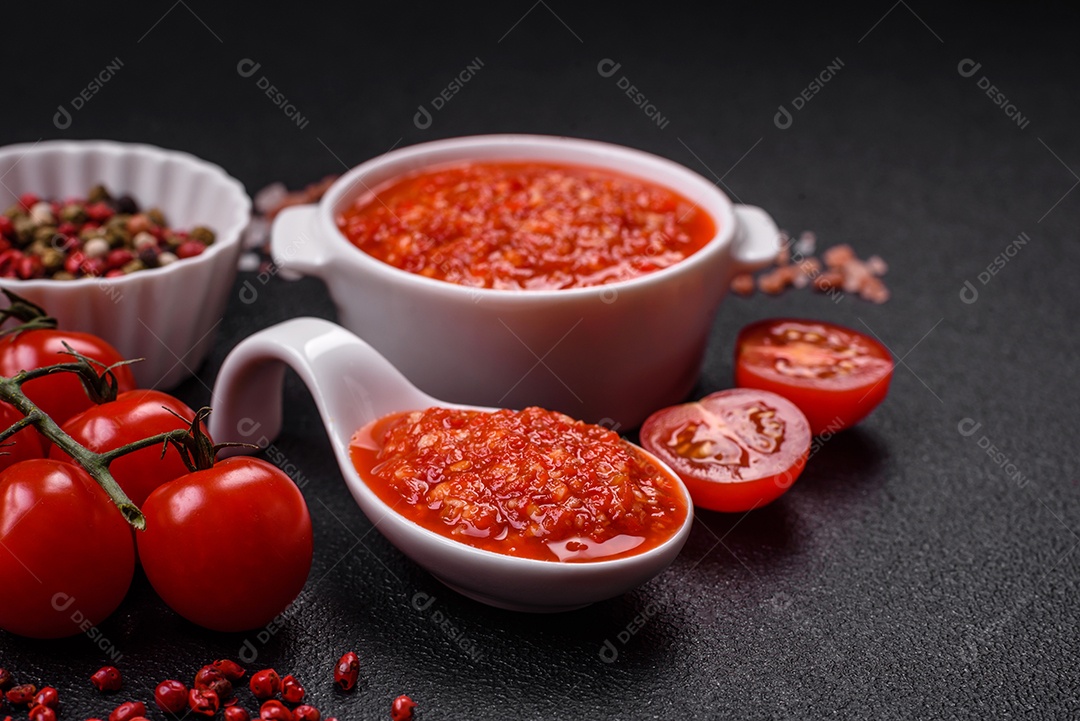 Delicioso molho vermelho picante com sal e especiarias em uma tigela de cerâmica sobre um fundo escuro de concreto
