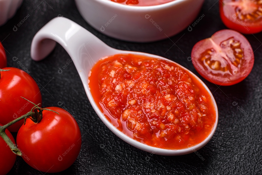 Delicioso molho vermelho picante com sal e especiarias em uma tigela de cerâmica sobre um fundo escuro de concreto