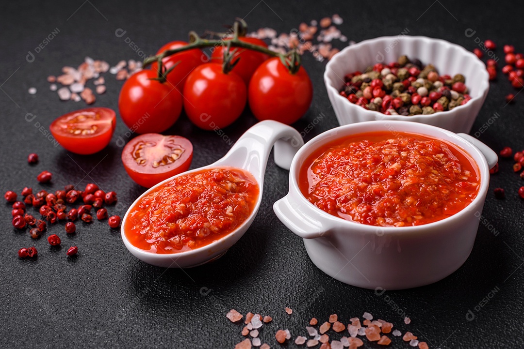 Delicioso molho vermelho picante com sal e especiarias em uma tigela de cerâmica sobre um fundo escuro de concreto