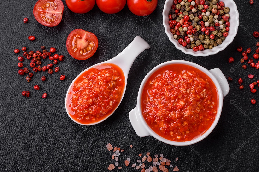 Delicioso molho vermelho picante com sal e especiarias em uma tigela de cerâmica sobre um fundo escuro de concreto