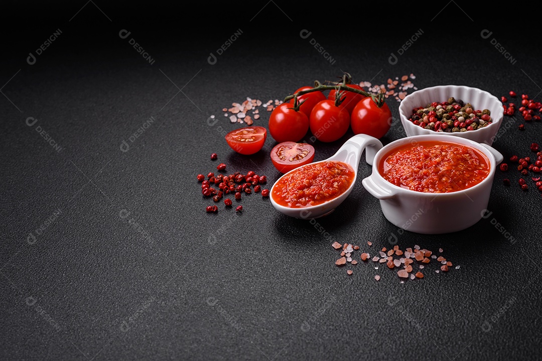 Delicioso molho vermelho picante com sal e especiarias em uma tigela de cerâmica sobre um fundo escuro de concreto