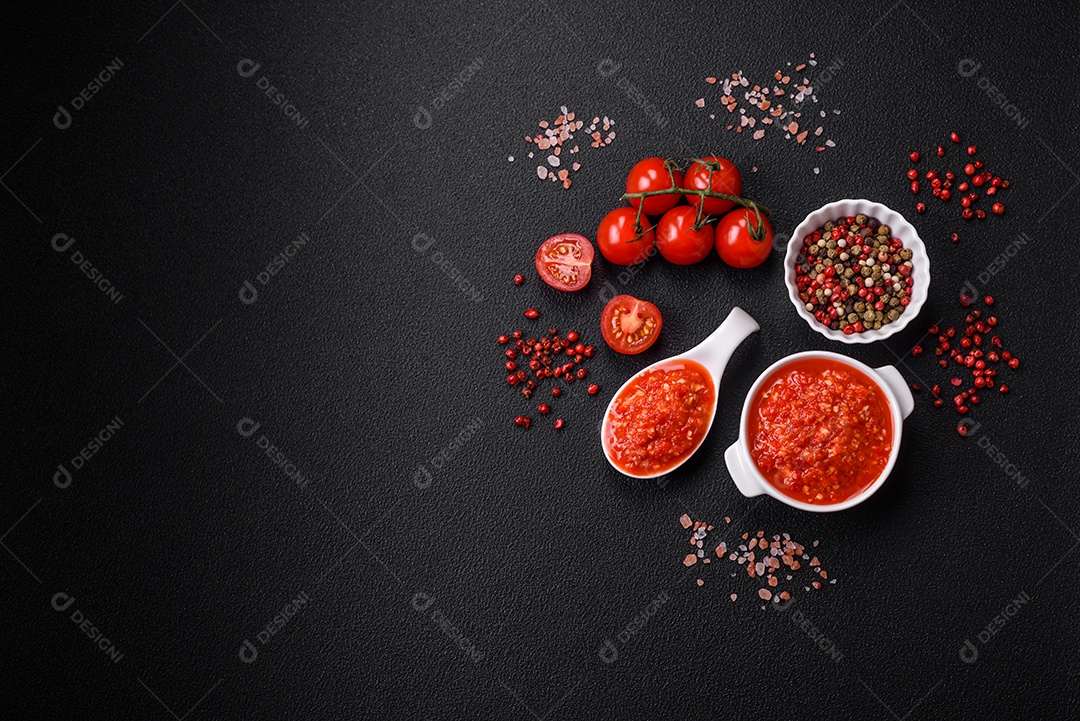 Delicioso molho vermelho picante com sal e especiarias em uma tigela de cerâmica sobre um fundo escuro de concreto