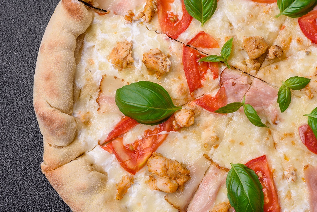 Deliciosa pizza quente com frango, tomate, queijo e bacon, com sal e especiarias e sobre fundo escuro de concreto