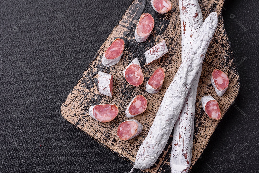 Delicioso fuet de linguiça defumada espanhola com sal e especiarias sobre um fundo escuro de concreto