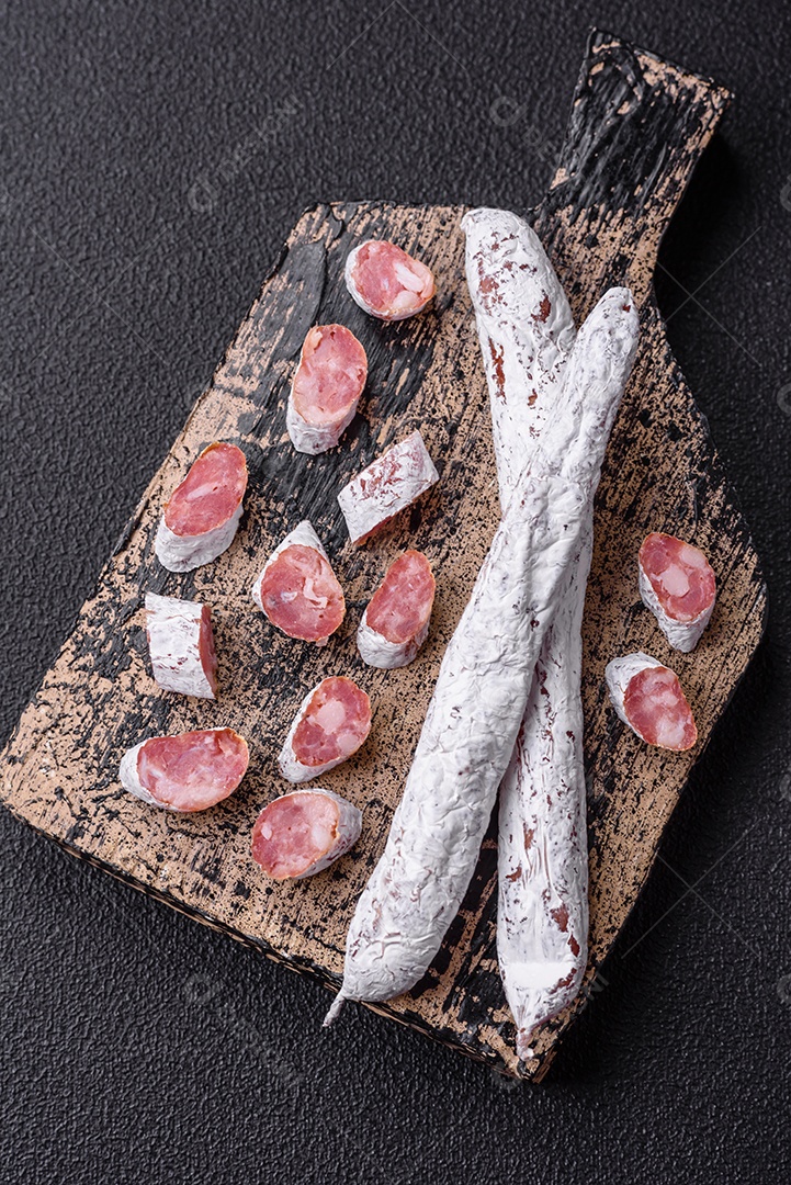 Delicioso fuet de linguiça defumada espanhola com sal e especiarias sobre um fundo escuro de concreto