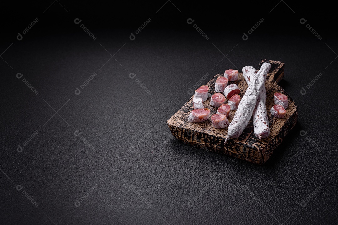 Delicioso fuet de linguiça defumada espanhola com sal e especiarias sobre um fundo escuro de concreto