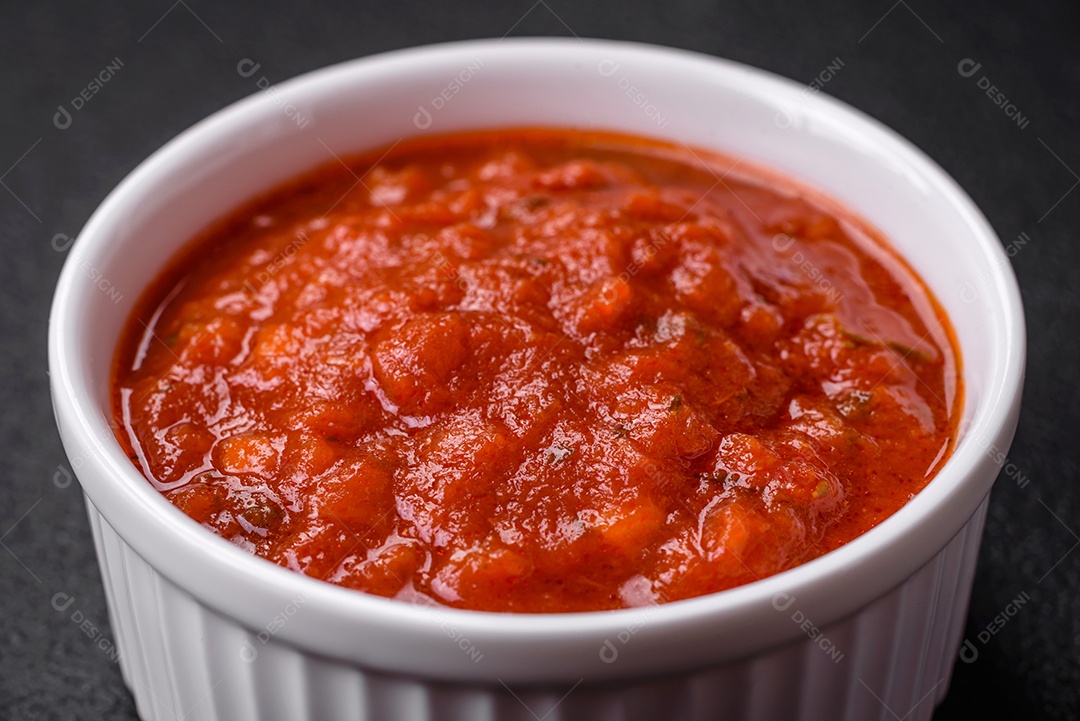 Delicioso molho Napoletana vermelho com cebola, sal, especiarias e ervas em uma tigela branca sobre fundo escuro de concreto