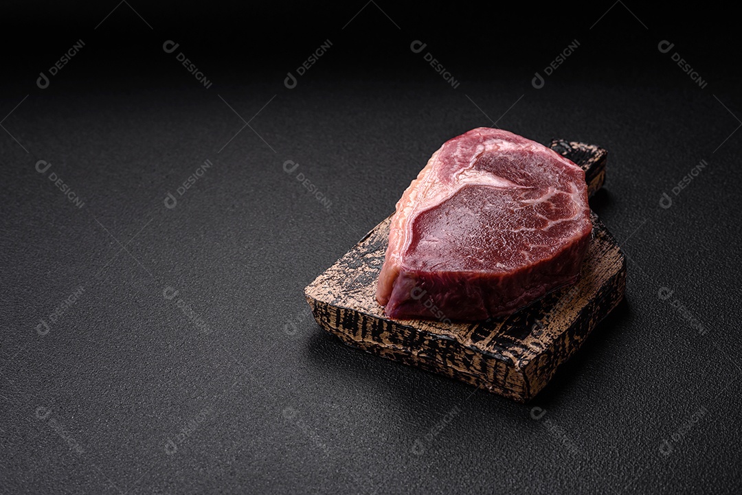 Bife de carne crua fresca com sal, especiarias e ervas sobre um fundo escuro de concreto