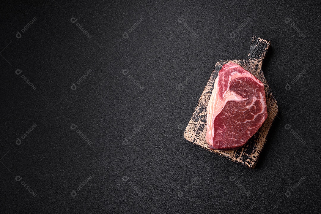 Bife de carne crua fresca com sal, especiarias e ervas sobre um fundo escuro de concreto