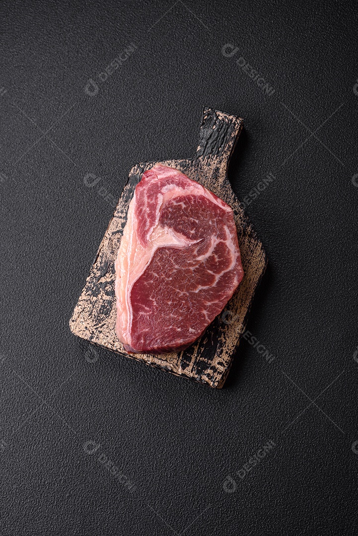 Bife de carne crua fresca com sal, especiarias e ervas sobre um fundo escuro de concreto