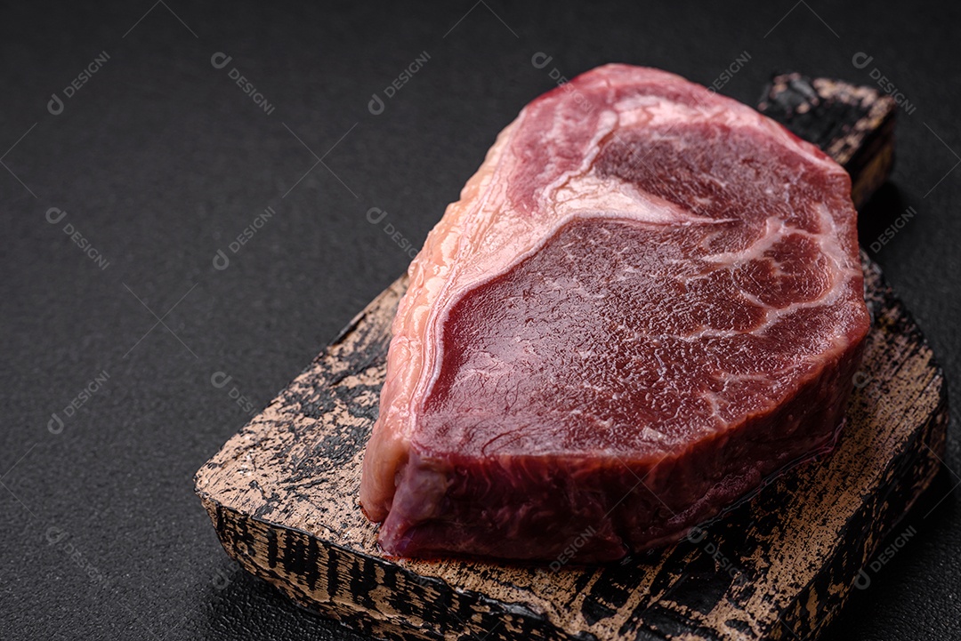 Bife de carne crua fresca com sal, especiarias e ervas sobre um fundo escuro de concreto